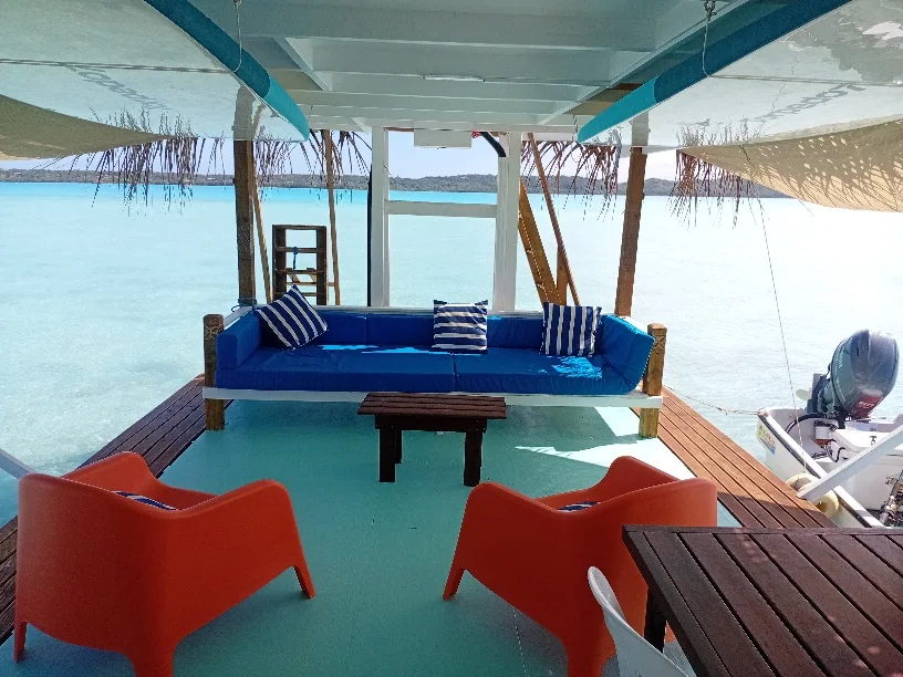 Open-air seating on the floating lounge, with blue lagoon water visible beyond the shaded deck.